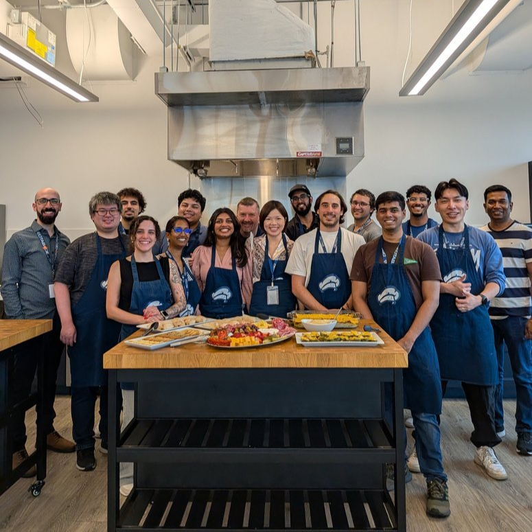 Abdulla Qeblawi and his Geotab team smiling together at a cooking class, gathered around a kitchen island with food they prepared.